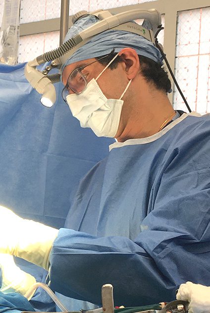 A surgeon in blue scrubs and mask holding surgical instruments.