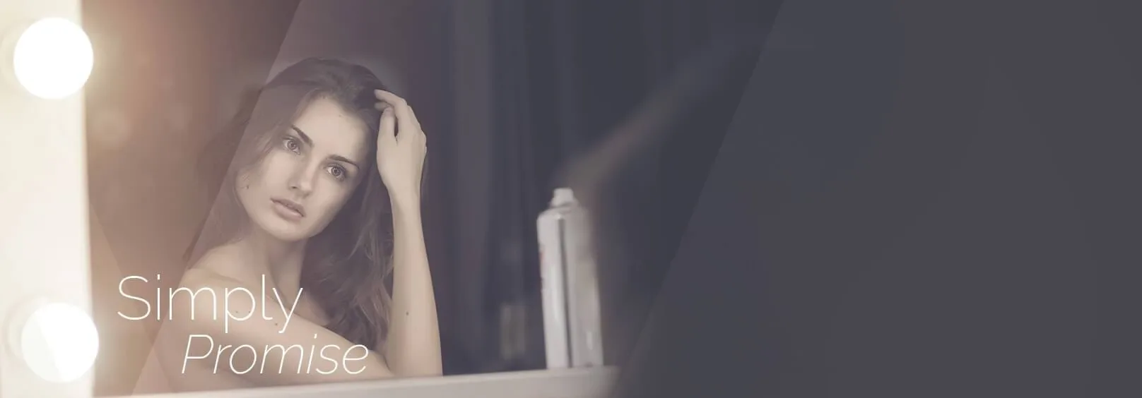 A woman sitting in front of a mirror spraying water on her face.