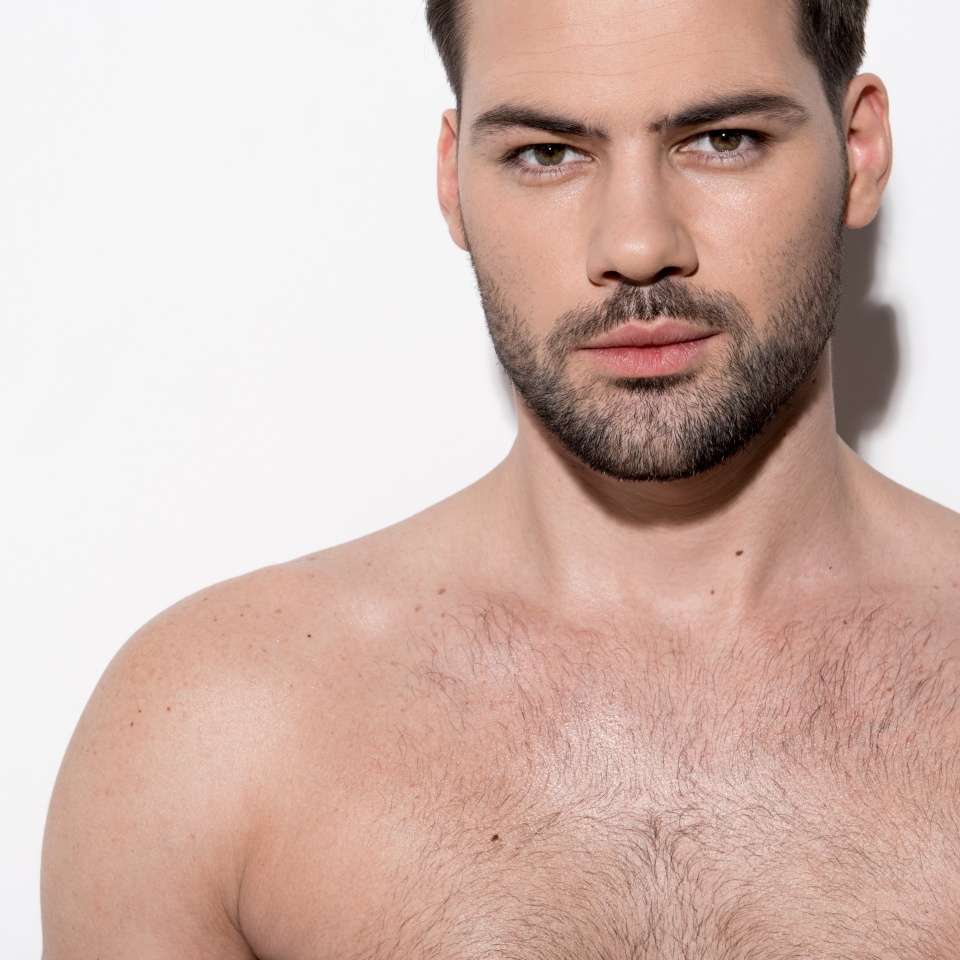 Healthy and beauty concept. Portrait of gorgeous cute bearded guy is standing against light background and looking at camera seductively
