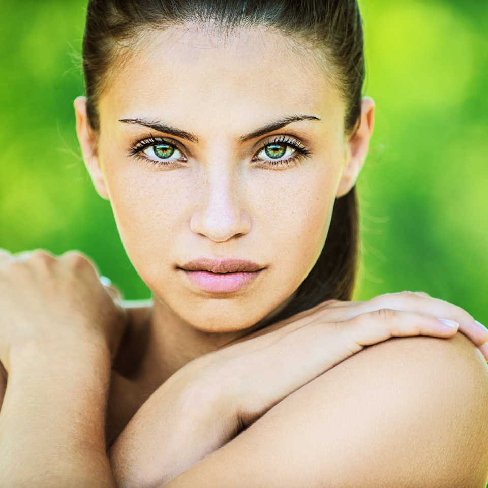 Portrait of young beautiful woman with bare shoulders crossed her arms, on green background summer nature.