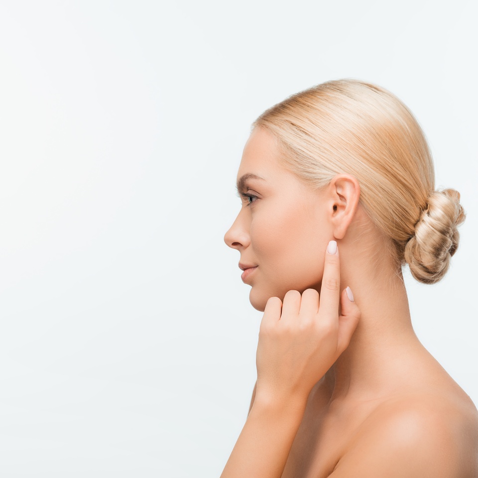 side view of naked young woman pointing with finger at ear isolated on white