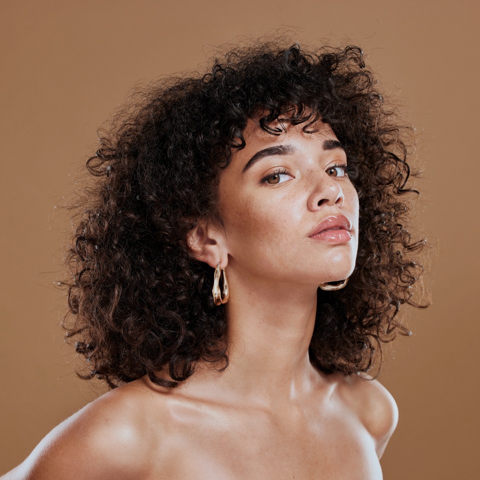 Black woman, beauty and skincare face portrait for natural afro, facial or hair care cosmetics. Healthy, beautiful and assertive model with curly hair shine and texture in brown studio background.