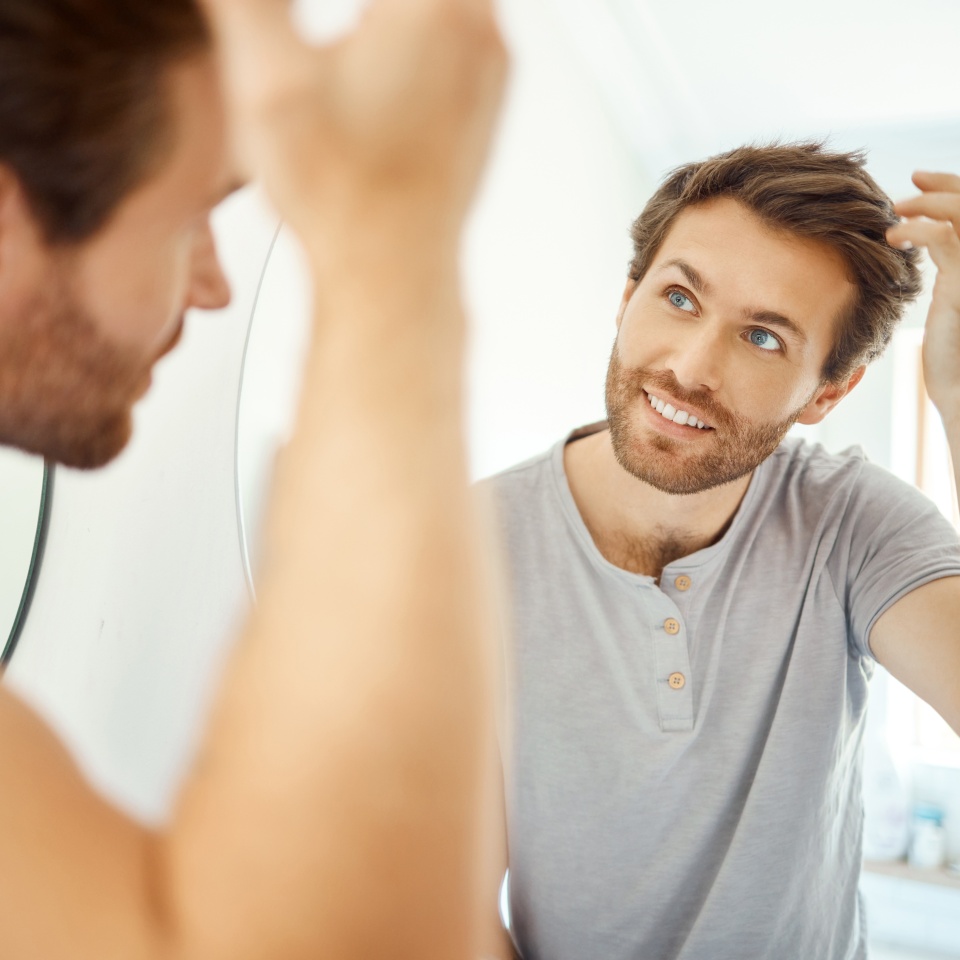 Bathroom, mirror reflection and happy man with hair care routine for maintenance, beauty process or hygiene cleaning treatment. Smile, morning and home person style locks for clean shampoo hairstyle